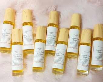 Könnte beinhalten: Zehn kleine Glasflaschen mit Holzverschlüssen, gefüllt mit einer gelben Flüssigkeit. Die Flaschen sind mit "Turmeric/Lemon Brightener" beschriftet und listen Zutaten wie Kurkuma, Zitrone und Sonnenblumenöl auf.