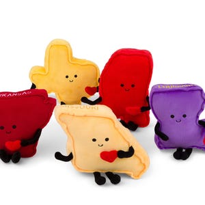 Puede incluir: Un conjunto de peluches con forma de estados de EE. UU., incluyendo Arkansas, Texas, Luisiana y Missouri. Cada peluche tiene una cara sonriente, extremidades negras y un coraz&oacute;n rojo. Los nombres de los estados est&aacute;n bordados.