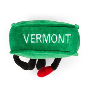 May include: Green plush toy shaped like a Vermont state with the word "VERMONT" embroidered in white on the front. The toy has black legs and red feet.