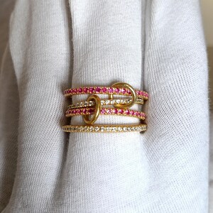 Puede incluir: Un conjunto de anillos de oro con varios dise&ntilde;os. Algunos anillos est&aacute;n adornados con piedras preciosas rosas, mientras que otros presentan piedras preciosas claras. Los anillos est&aacute;n entrelazados con bucles dorados, creando un aspecto &uacute;nico y elegante.