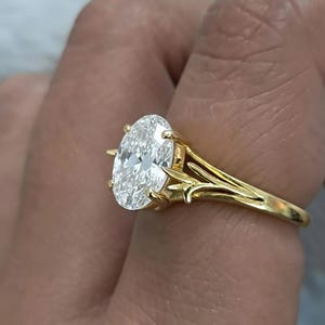 Può includere: Un anello di fidanzamento in oro con un diamante taglio ovale. L'anello presenta un design a gambo diviso con accenti decorativi. Il diamante è incastonato con griffe. Il design è elegante.