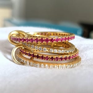 Puede incluir: Un conjunto de anillos dorados con filas alternas de piedras rojas y transparentes. Los anillos est&aacute;n entrelazados, creando un dise&ntilde;o &uacute;nico y elegante. Las piedras preciosas brillan, a&ntilde;adiendo un toque de lujo a la joyer&iacute;a.