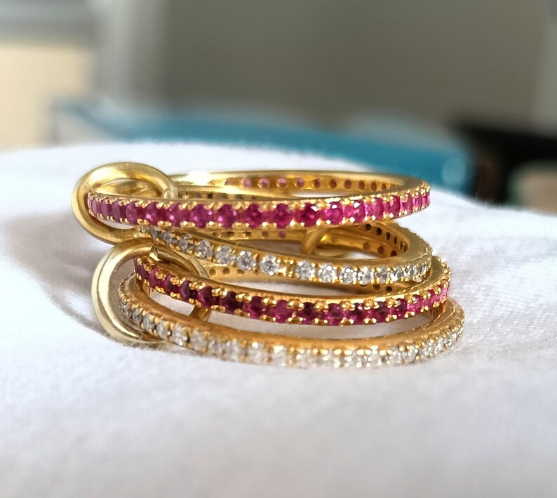 Puede incluir: Un conjunto de anillos dorados con filas alternas de piedras rojas y transparentes. Los anillos est&aacute;n entrelazados, creando un dise&ntilde;o &uacute;nico y elegante. Las piedras preciosas brillan, a&ntilde;adiendo un toque de lujo a la joyer&iacute;a.