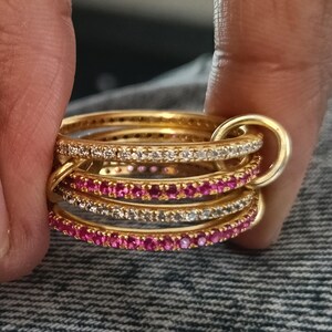 Puede incluir: Un conjunto de anillos dorados, algunos con piedras preciosas claras y rosas. Los anillos est&aacute;n unidos por un anillo dorado m&aacute;s grande. Las piedras est&aacute;n dispuestas en una l&iacute;nea continua.