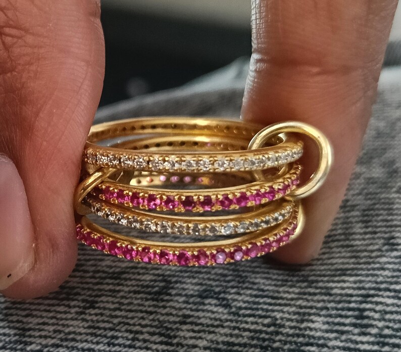 Puede incluir: Un conjunto de anillos dorados, algunos con piedras preciosas claras y rosas. Los anillos est&aacute;n unidos por un anillo dorado m&aacute;s grande. Las piedras est&aacute;n dispuestas en una l&iacute;nea continua.