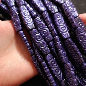 May include: A strand of dark purple glass beads with a swirl design. The beads are smooth and shiny.