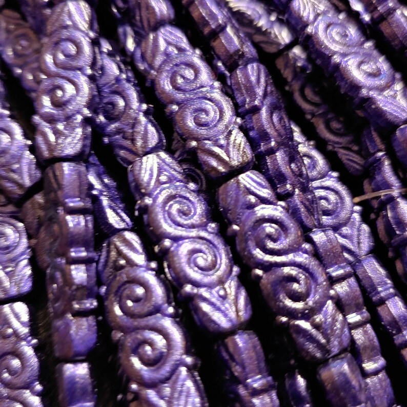 May include: A close-up of a strand of purple glass beads with a swirling design. The beads are arranged in a row and have a shiny, metallic finish.