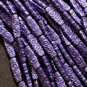 May include: A close-up of a strand of purple glass beads with a swirl design. The beads are all the same size and shape, and they are arranged in a row.