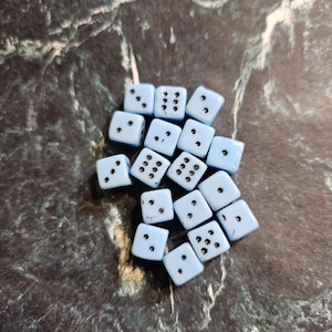 May include: A group of 15 light blue dice with black dots. The dice are scattered on a dark gray marble surface.