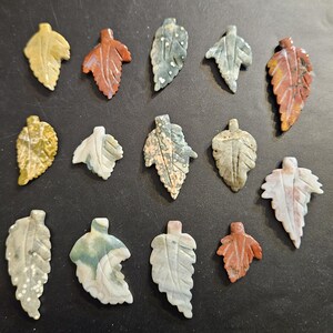 May include: Assortment of 15 carved stone leaf pendants in various colors and patterns, including green, brown, white, and red.