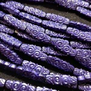 May include: A close-up of a strand of purple glass beads with a swirling pattern. The beads are arranged in a row and are all the same size and shape.