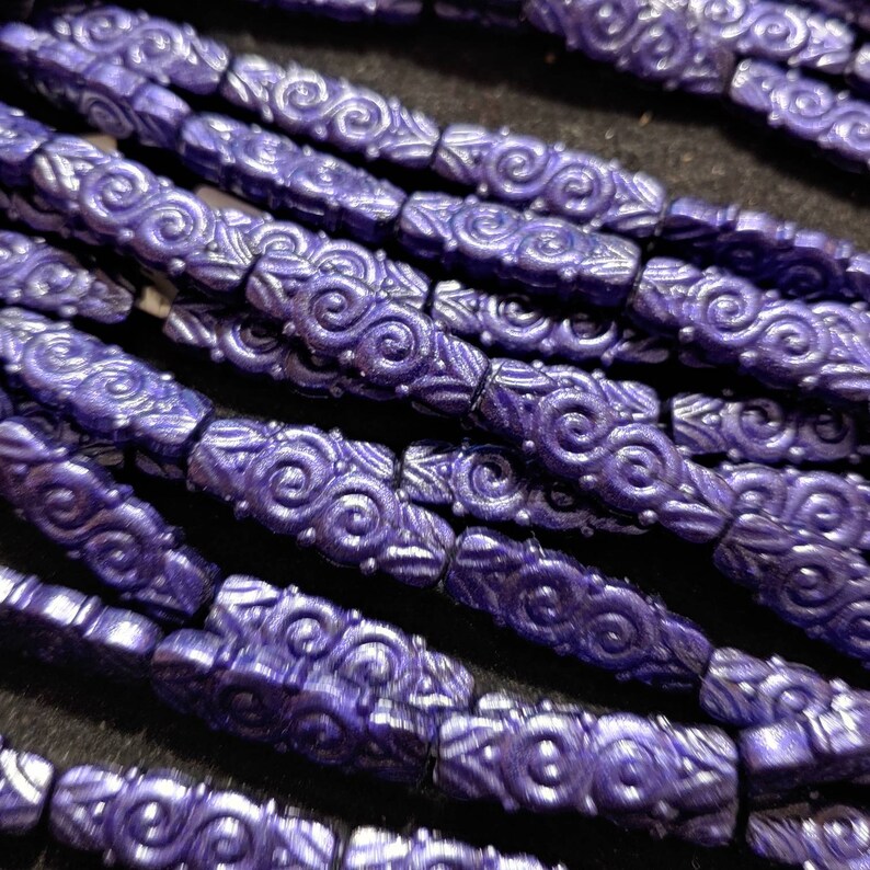 May include: A close-up of a strand of purple glass beads with a swirling pattern. The beads are arranged in a row and are all the same size and shape.