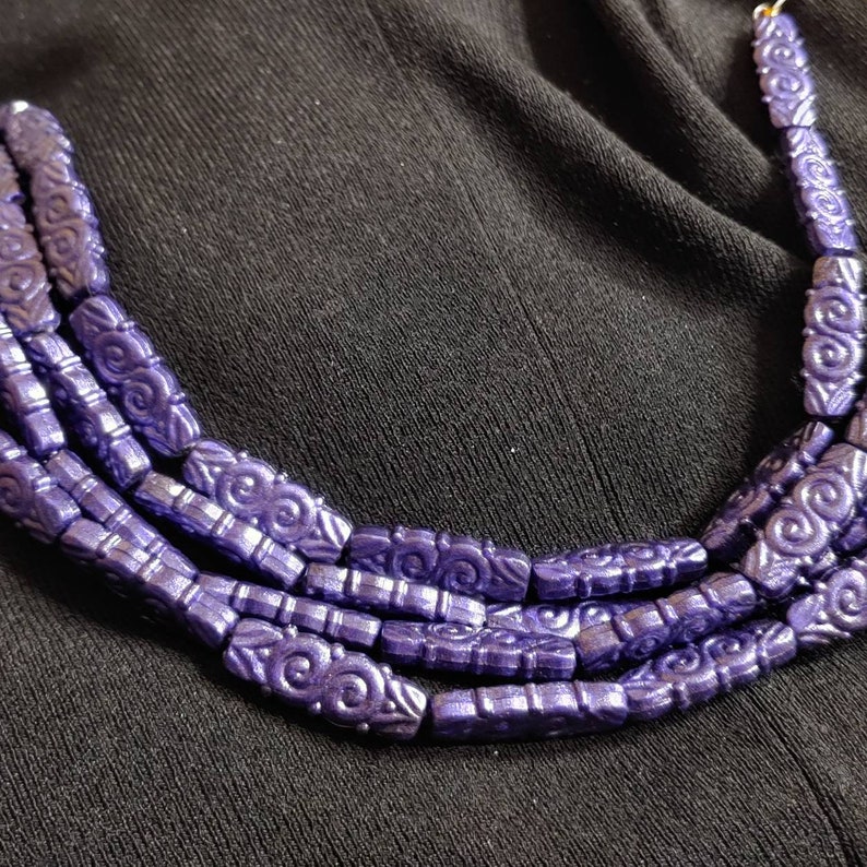 May include: A multi-strand necklace made of dark purple beads with a swirling pattern. The beads are connected by a gold thread.