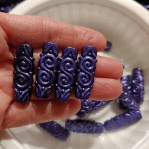 May include: Four dark purple, decorative, rectangular beads with a swirling pattern. The beads are made of a smooth, shiny material.