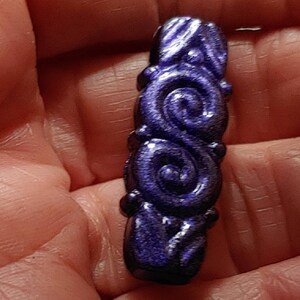 May include: A dark purple, metallic, decorative pendant with a swirling, ornate design.