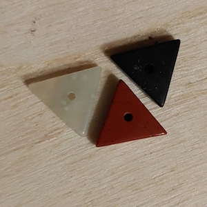 May include: Three triangular stone beads with holes in the center. The beads are white, black, and red.
