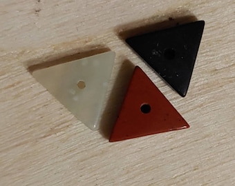 May include: Three triangular stone beads with holes in the center. The beads are white, black, and red.