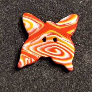 May include: A red, white, and yellow swirl patterned butterfly-shaped button. The button has two holes for sewing.