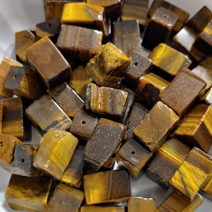 May include: A collection of brown and gold tiger's eye gemstone beads. The beads are all rectangular in shape and have a smooth, polished finish.