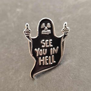 Peut inclure: Une épingle en émail noir et argent représentant un fantôme avec un visage de crâne faisant un doigt d'honneur avec les deux mains. Le fantôme est entouré d'argent et porte l'inscription "See you in hell" sur sa poitrine.
