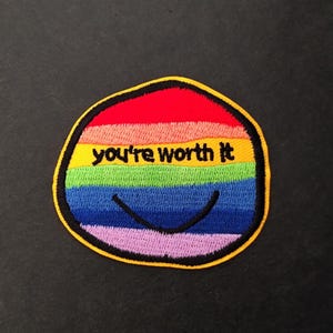 Può includere: Toppa ricamata colorata con un design arcobaleno e la scritta "you're worth it". La toppa ha un bordo giallo e una faccina sorridente. I colori includono rosso, arancione, giallo, verde, blu e viola.