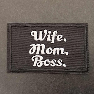 Op de afbeelding: Zwarte geborduurde patch met witte tekst die "Wife, Mom, Boss." luidt.
