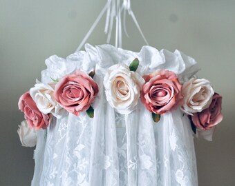 May include: White lace canopy with a circle of pink and white fabric roses around the top.