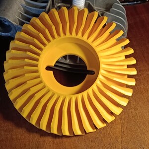 Könnte beinhalten: Ein leuchtend gelbes, kreisförmiges Schleifrad mit radialen Lamellen. Das Rad hat eine zentrale Öffnung und liegt auf einer Holzoberfläche. Eine metallische Komponente ist teilweise im Hintergrund zu sehen.