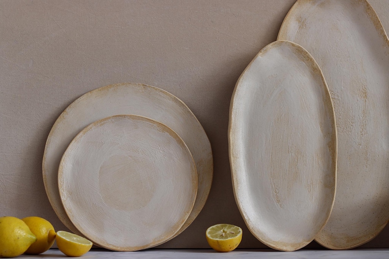 In front of one wall are two plates, a dinner plate and a dessert plate, and two oval platters in matte white glazed stoneware.