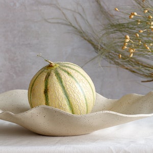 A very large beige ceramic marbled fruit bowl contains a melon. Light mood photo.