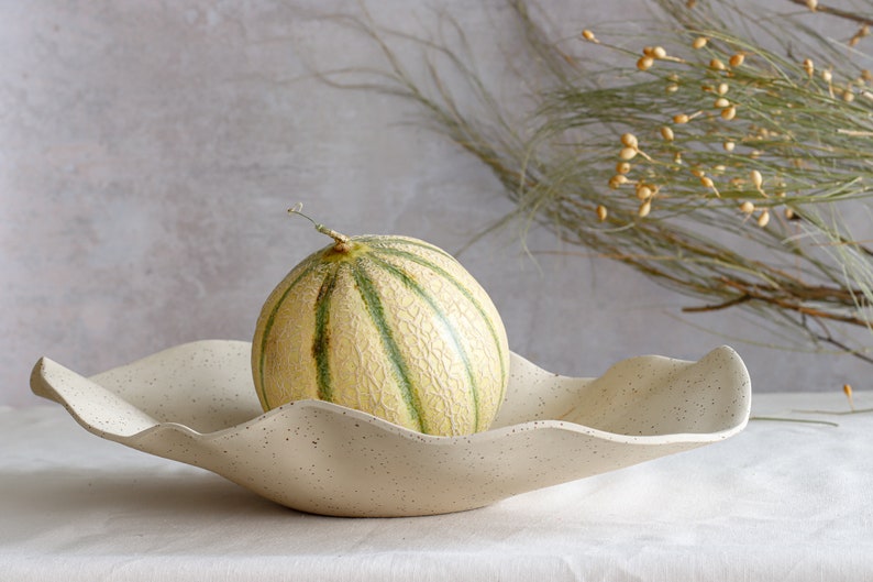 A very large beige ceramic marbled fruit bowl contains a melon. Light mood photo.