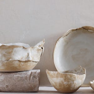 Op de afbeelding: Een set van drie keramische mokken met een gespikkelde, matte afwerking. De mokken zijn in tinten crème, lichtgrijs en donkergrijs. Elke mok heeft een eenvoudig, minimalistisch ontwerp, perfect voor koffie of thee.