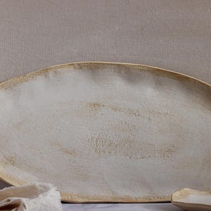 Close-up view of a very rustic, oval-shaped, matte white stoneware tray.