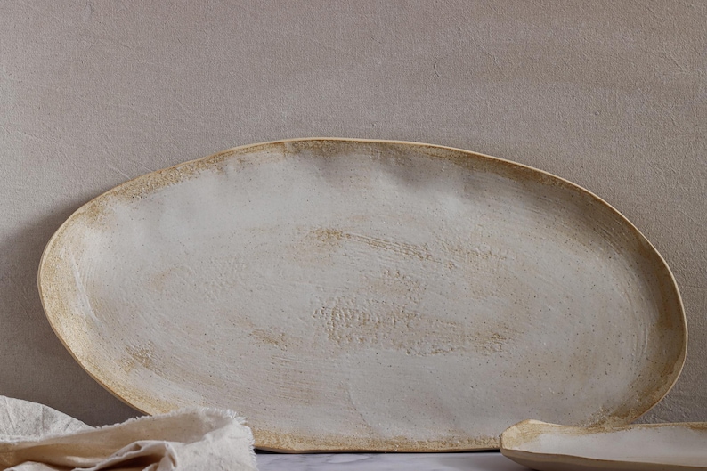 Close-up view of a very rustic, oval-shaped, matte white stoneware tray.