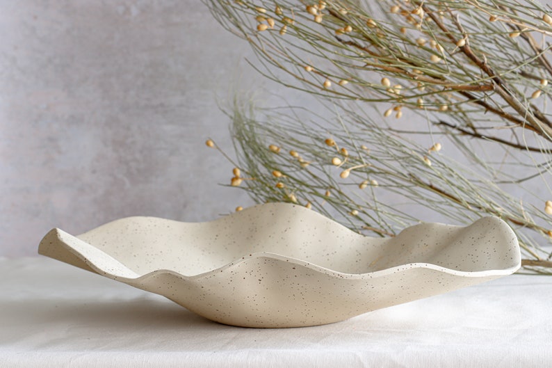 Very large centerpiece made of mottled beige stoneware with a wavy shape.