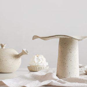 Still life scene. High-key photo. On the right is a beige mottled stoneware cake stand. On the left in the background is a teapot of the same material. There are also small plates containing sweet desserts.