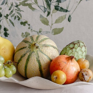 Light mood photo. Large centerpiece. It is made of beige-marbled ceramic and contains several fruits.