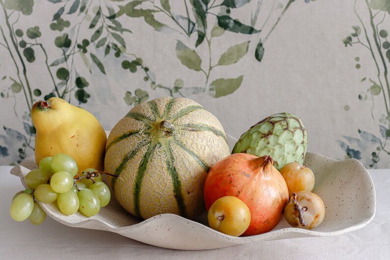 Light mood photo. Large centerpiece. It is made of beige-marbled ceramic and contains several fruits.