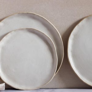 Puede incluir: Un juego de tres tazas de cerámica con un acabado moteado y mate. Las tazas son de color crema, gris claro y gris oscuro. Cada taza tiene un diseño simple y minimalista.