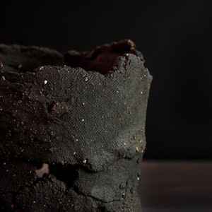 Dark mood photo. Detail of the utensil holder. You can see a lot of texture and holes strategically made to make the piece look rustic and primitive.