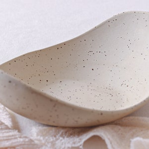 Front view of a fruit bowl seen diagonally. It is made of mottled beige clay and is deep and oval in shape.