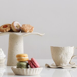 Still life scene. Light mood photo. On the right is a cup with a plate with wavy edges. On the left is a cake stand with cookies surrounded by small plates with waves containing macarons and other sweets.