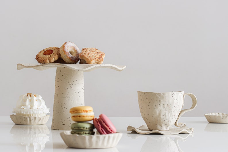 Still life scene. Light mood photo. On the right is a cup with a plate with wavy edges. On the left is a cake stand with cookies surrounded by small plates with waves containing macarons and other sweets.