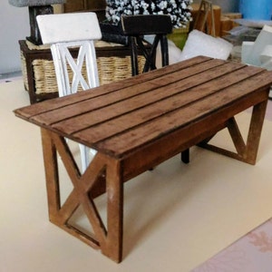 May include: A miniature wooden table with a brown wood top and a criss-cross design on the legs. The table is made of wood and has a rustic look.