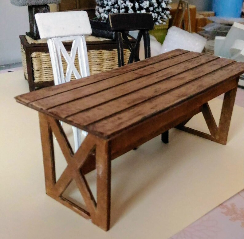 May include: A miniature wooden table with a brown wood top and a criss-cross design on the legs. The table is made of wood and has a rustic look.