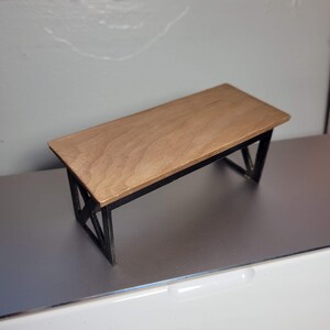May include: A small wooden table with a black metal frame. The table top is light brown and the frame is made of thin metal bars.