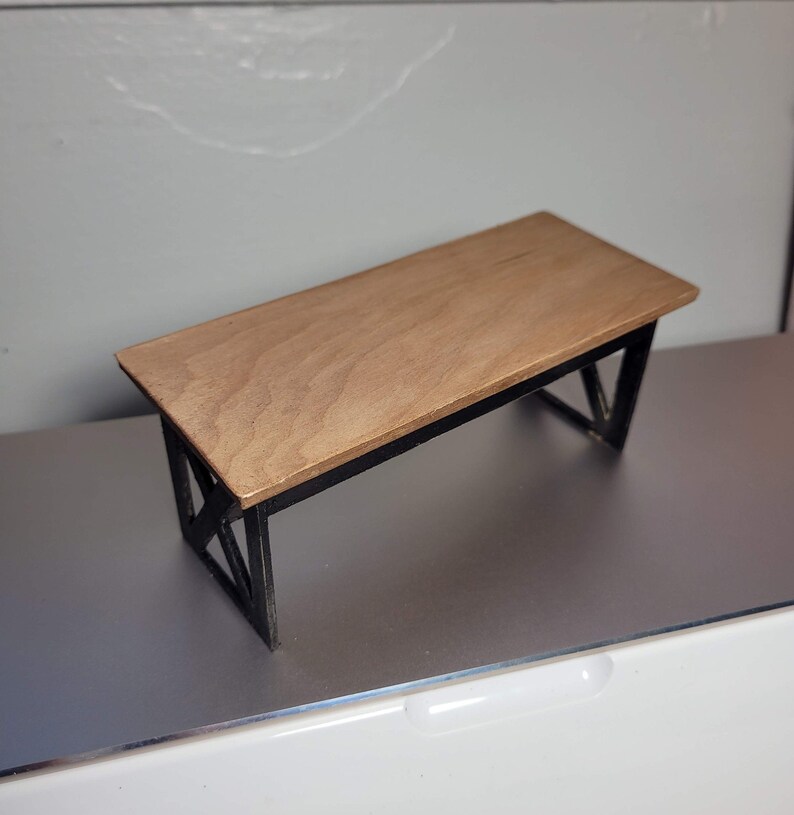 May include: A small wooden table with a black metal frame. The table top is light brown and the frame is made of thin metal bars.