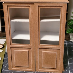 May include: A brown wooden cabinet with glass doors and two shelves. The cabinet has a simple design with a raised panel on each door.