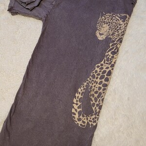 May include: A dark gray t-shirt featuring a tan leopard design. The distressed tee has a crew neck and short sleeves. The leopard graphic is on the front of the shirt.