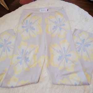 Puede incluir: Pantalones de punto lila claro con un estampado floral en amarillo y azul claro. Los pantalones tienen un dise&ntilde;o de pierna ancha y un ajuste c&oacute;modo y relajado. El estampado floral est&aacute; distribuido uniformemente por los pantalones. La etiqueta dice 'House of Sunny'.